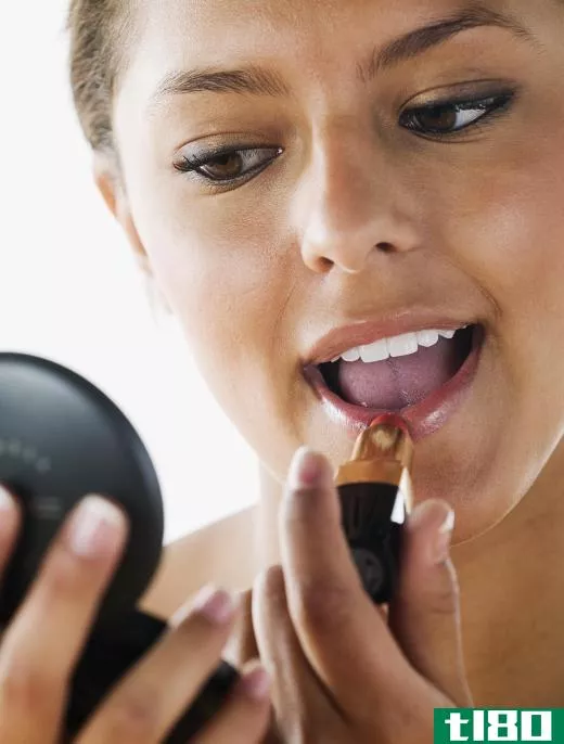 A brunette woman applies lipstick.