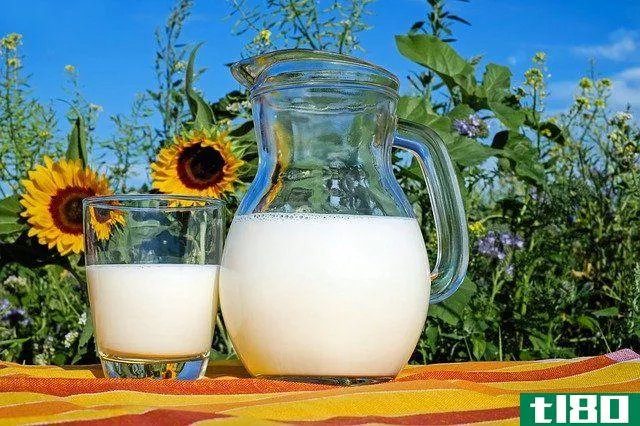 Milk jug and glass on wooden table in front of sunflowers