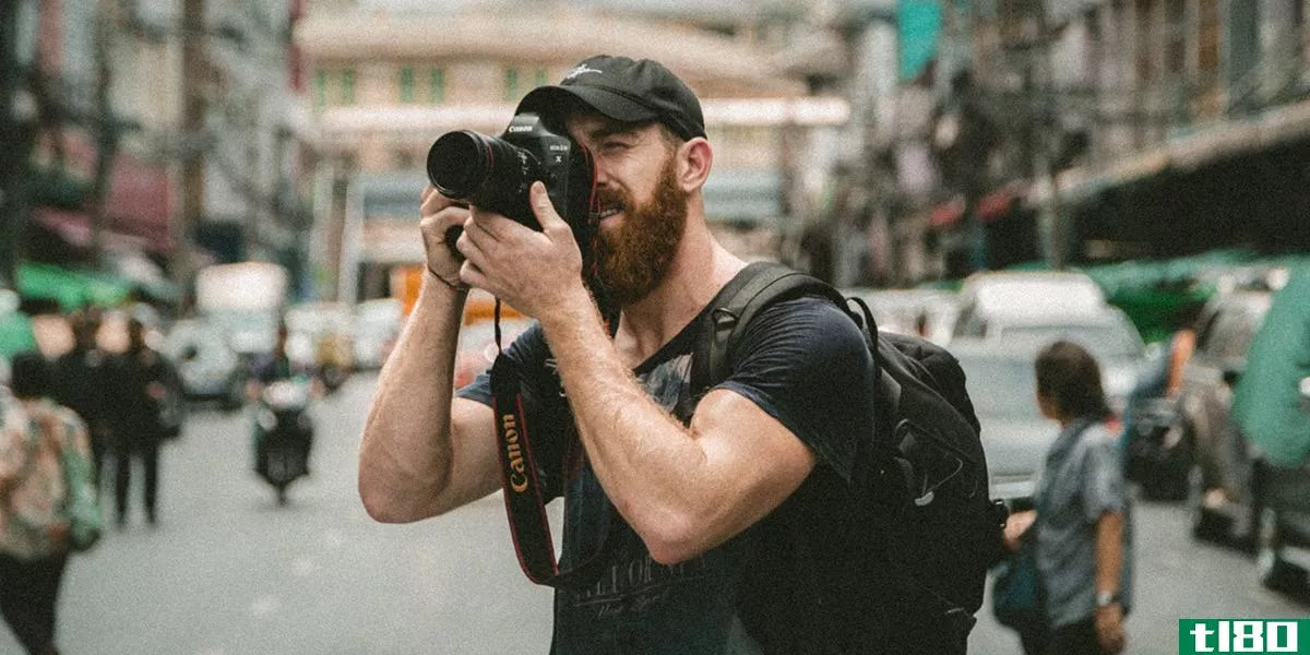 A bearded man taking a photo with a DSLR