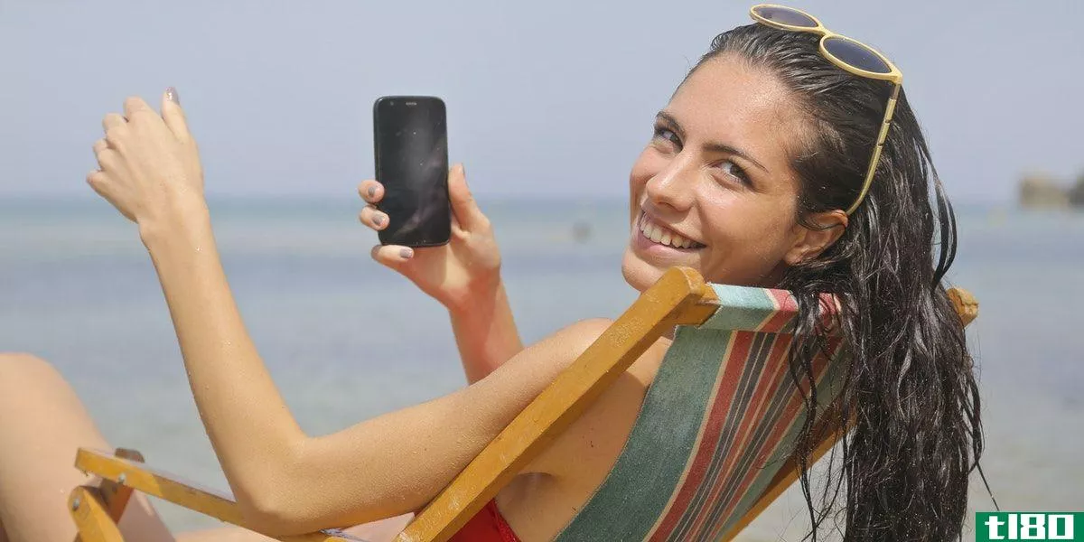 A woman half-turned in a chair at a beach **iling at the camera and holding her phone
