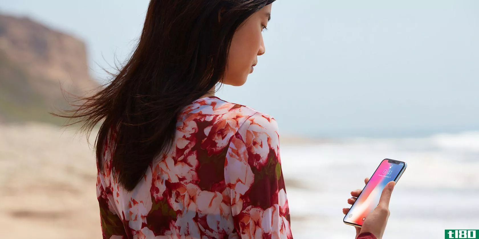 A photograph showing a young woman standing at the beach and looking at her iPhone X