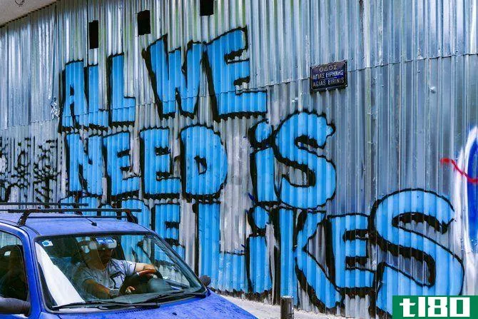 Car beside a wall of graffiti that reads "All We Need Is More Likes"