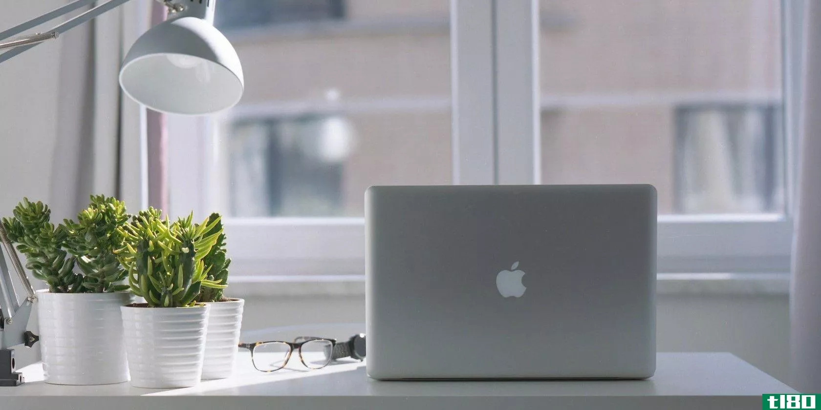 Macbook sitting on a desk with plants, eyeglasses, and a lamp