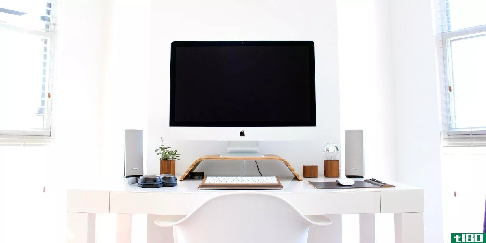 A photograph of a desktop iMac on an organised desk, in a white room with white furniture