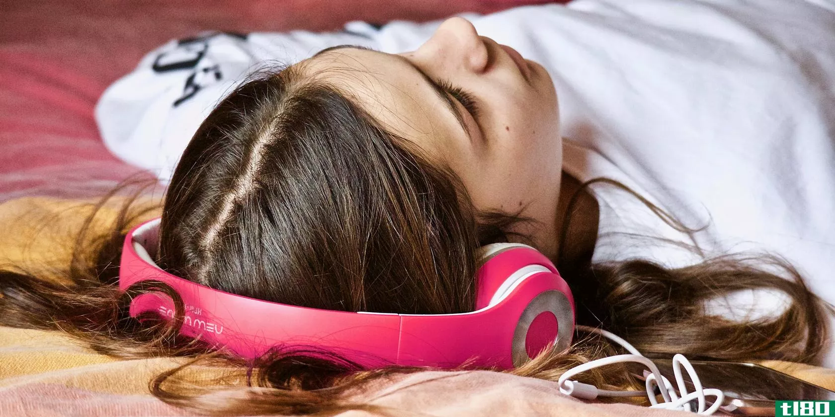 Girl laying on her back and wearing pink headphones