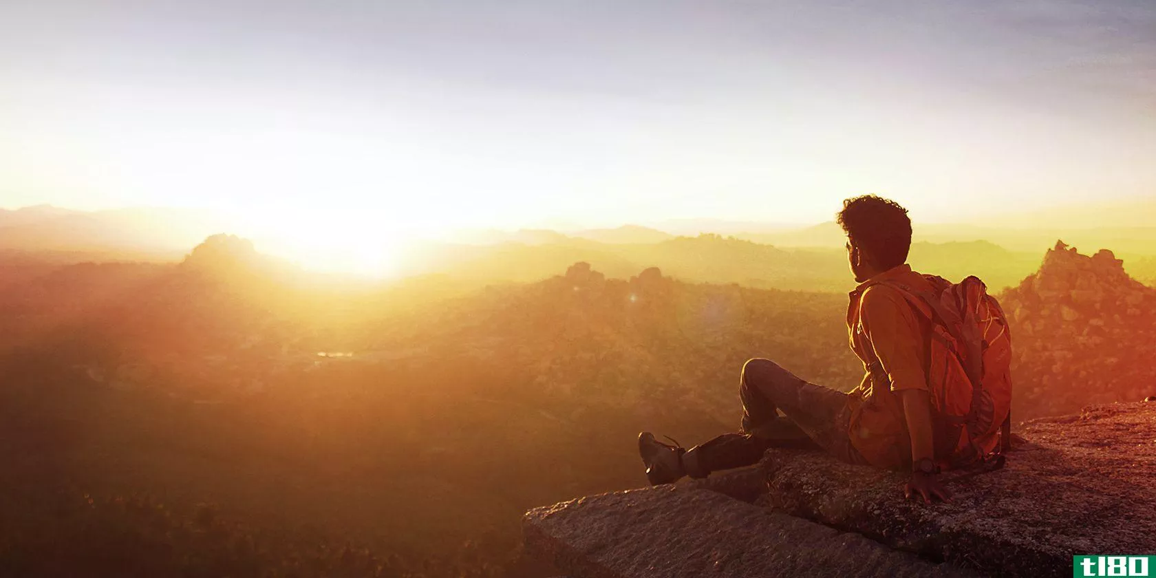 Man sitting on cliff facing sunset