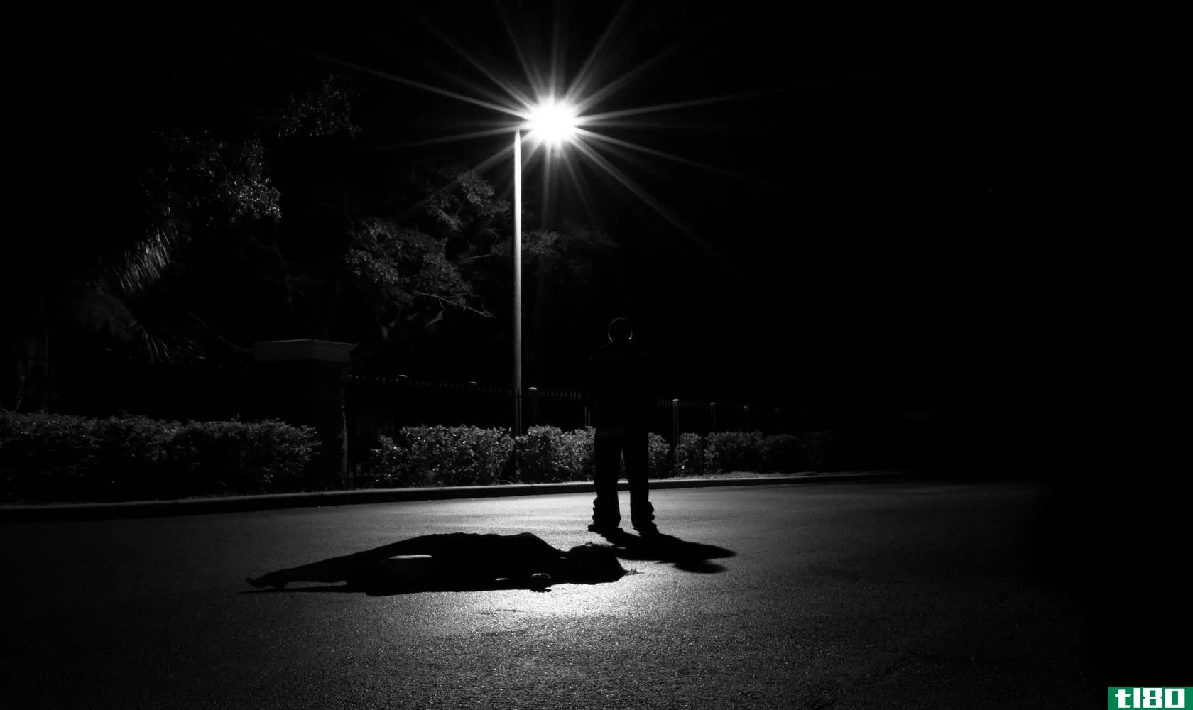Person outside standing in the dark above another person who is laying down 