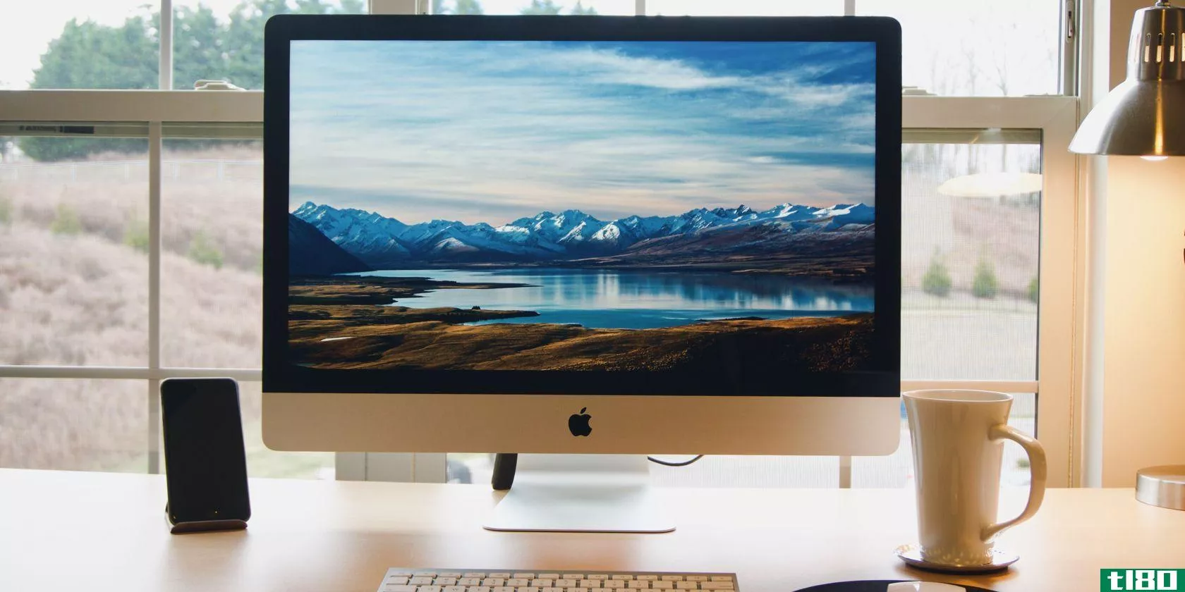 A photograph of an iMac sitting in front of a window framing a picturesque scene