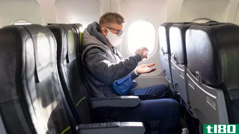 Person in mask on a plane, applying hand sanitizer. He has the row to himself.