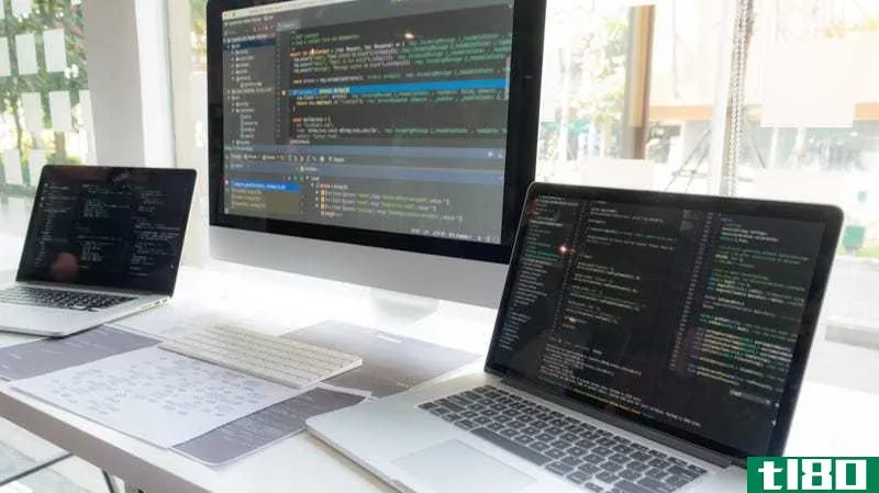 Two laptops and a computer on a desk, their screens displaying code
