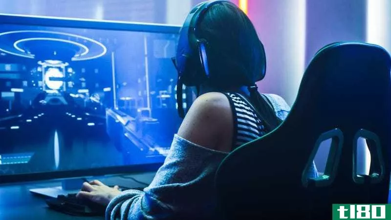 A woman sits at a computer playing a game while wearing a headset
