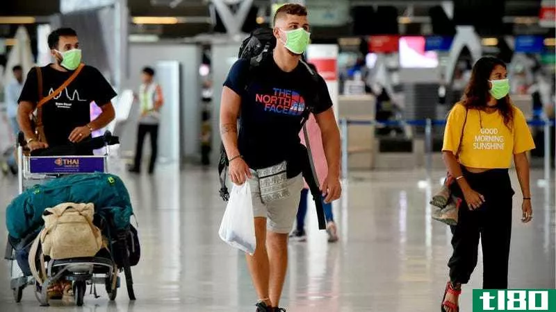 People wearing masks walk through an airport with their luggage.