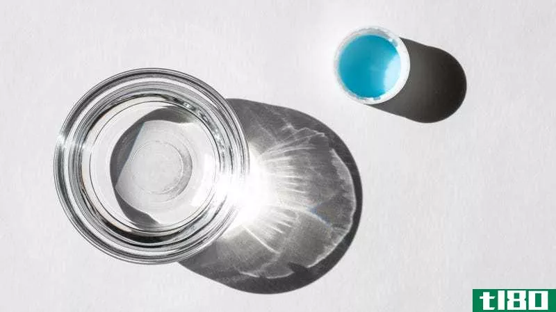 A **all clear glass bowl of distilled white vinegar and an upturned plastic bottle cap with a blue liner sit on a white background.
