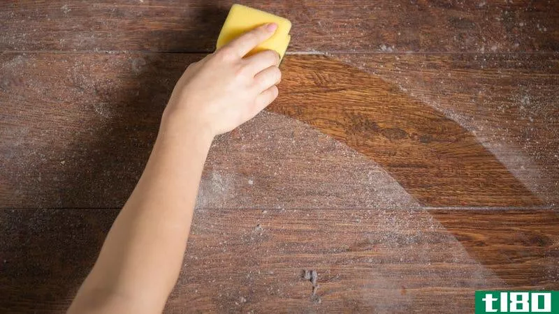 A person wipes dust off a wooden table with a yellow sponge