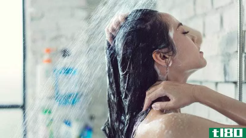 An Asian woman with light skin and dark hair stands under a shower with her eyes closed.