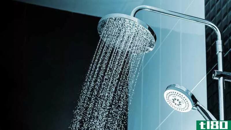 A round waterfall-style shower head sprays water in front of a light blue tiled wall. 