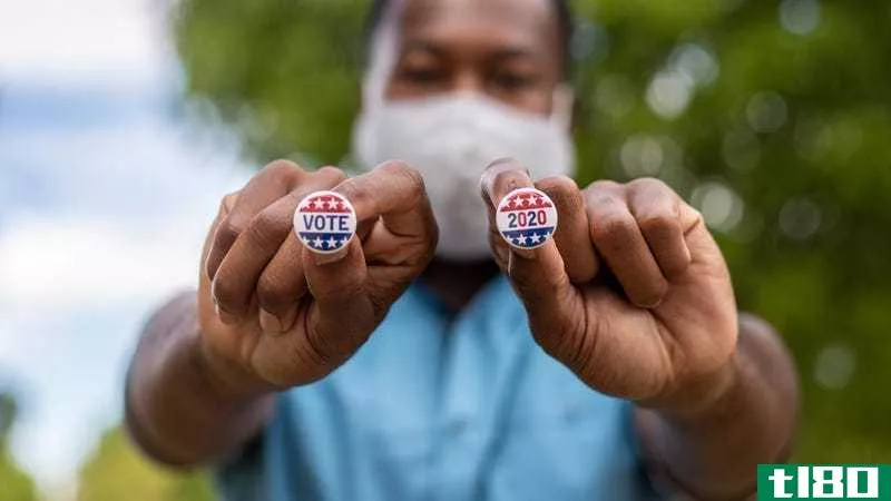 A man holds up two **all pins reading "Vote 2020"