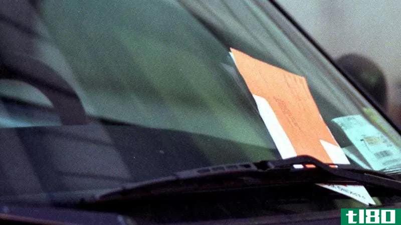 An orange parking ticket envelope under a windshield wiper